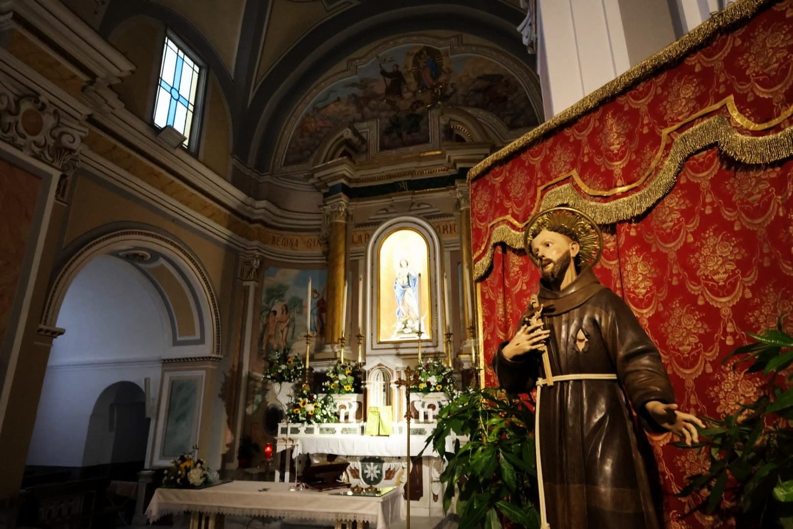 Statua lignea di un santo francescano davanti a un drappo rosso, nella chiesa di San Pasquale